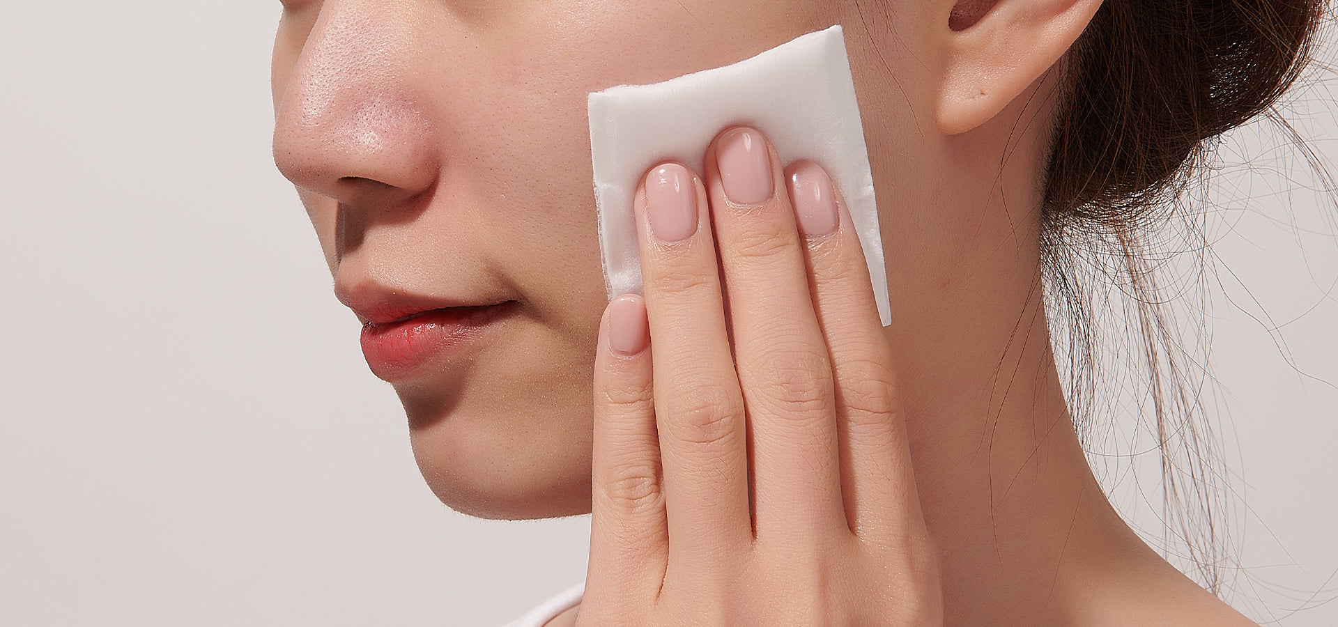 Close-up of a person applying a toner with a cotton pad to their cheek.