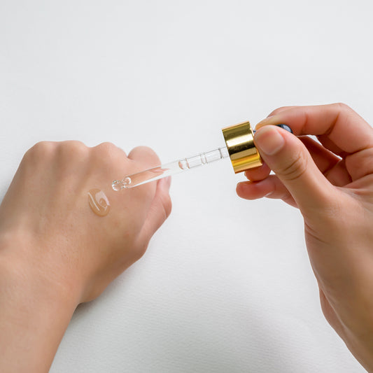 Hand applying Vitamin C Brightening Essence with a dropper onto skin.