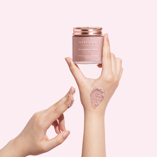 Hands showing a jar of Mary & May Rose Hyaluronic Hydra Wash off Pack with product applied on the back of one hand.
