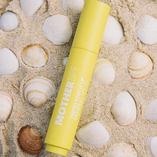 Mother SPF Tinted Touch Up Mineral SPF 50 stick on sandy beach with shells.