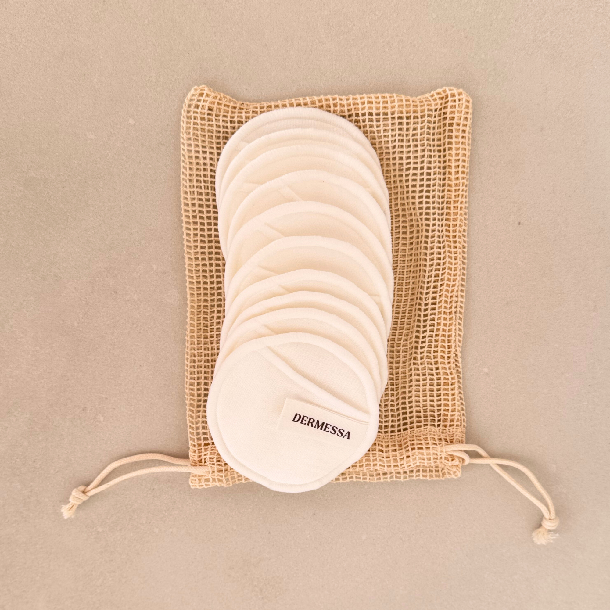Set of white cotton pads in a brown mesh bag on a beige background