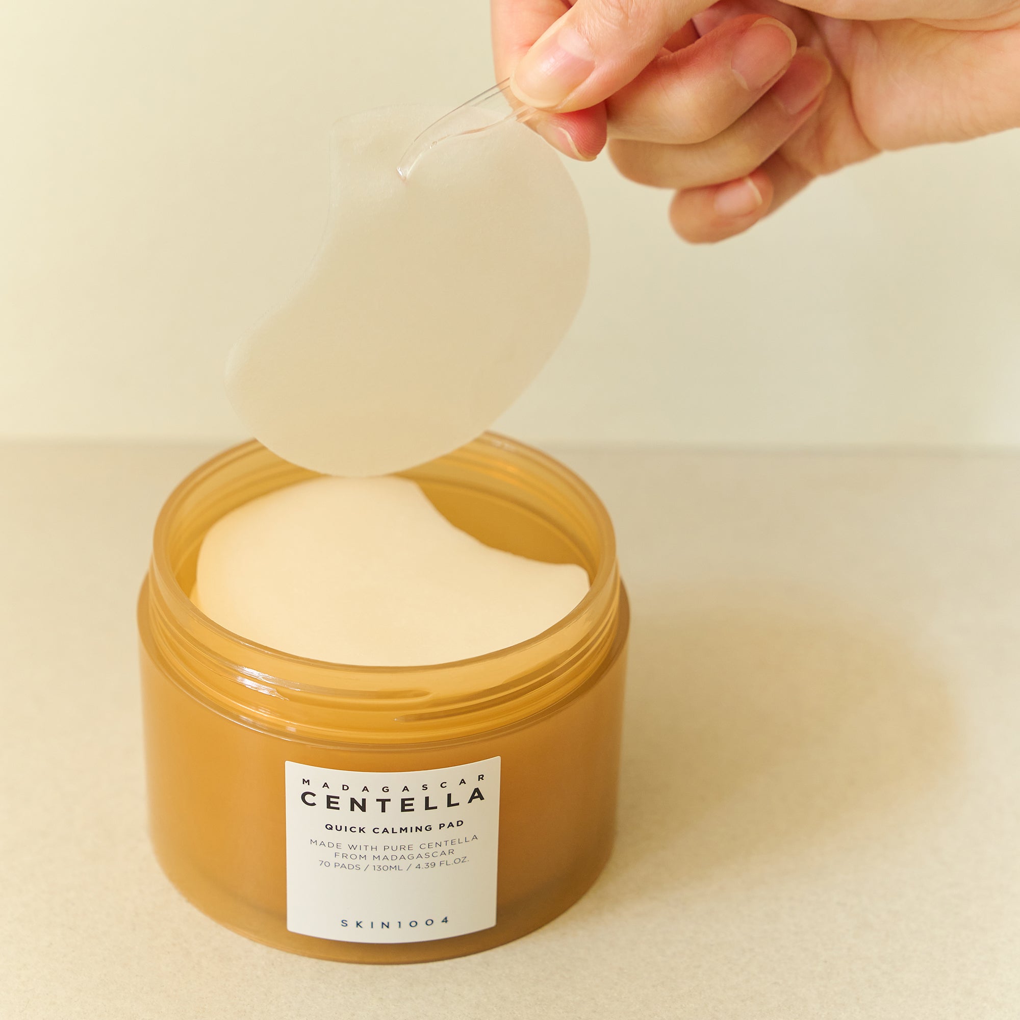 Hand holding a Madagascar Centella Quick Calming Pad above an open jar by SKIN1004.
