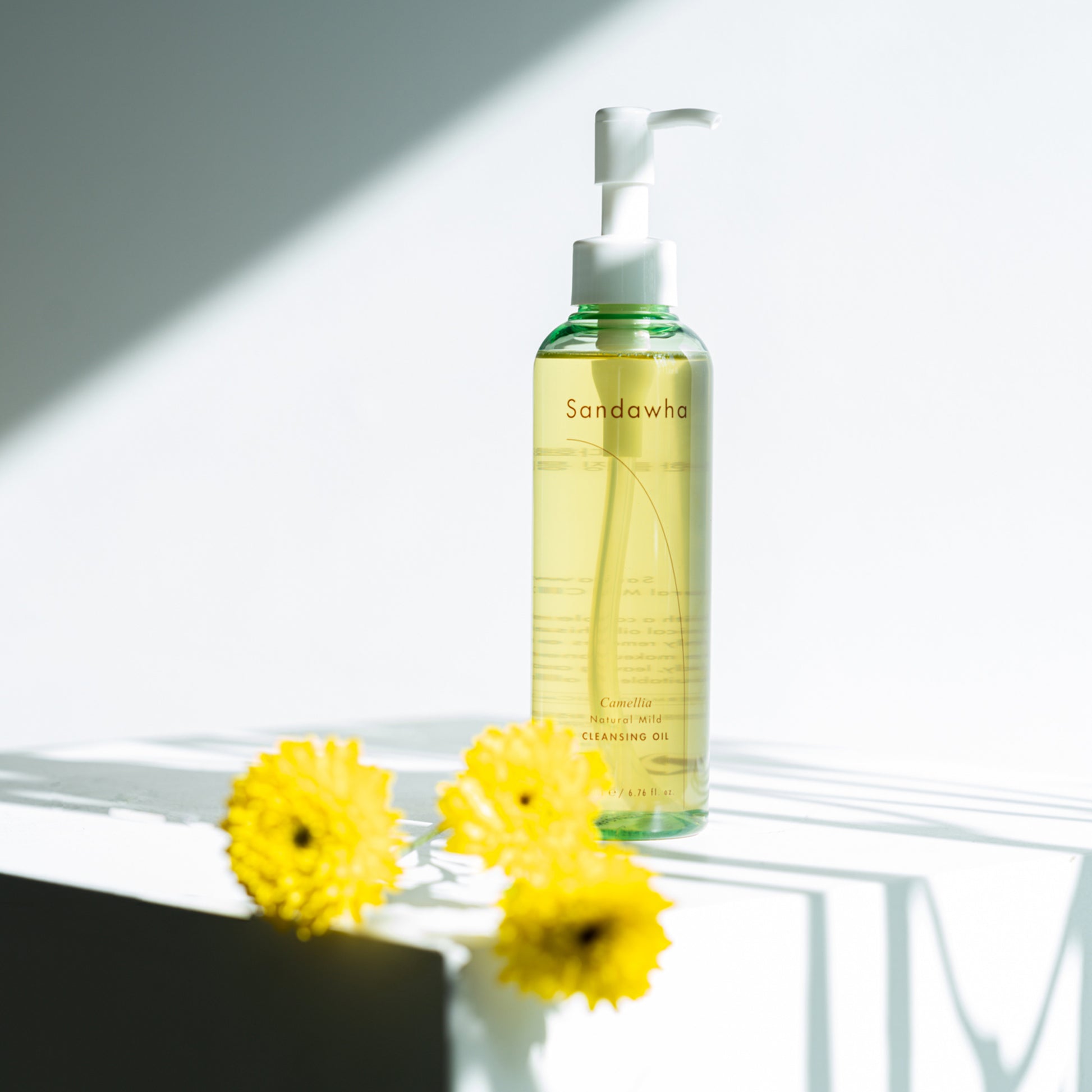 Sandawha Natural Mild Cleansing Oil bottle with yellow flowers in soft lighting.