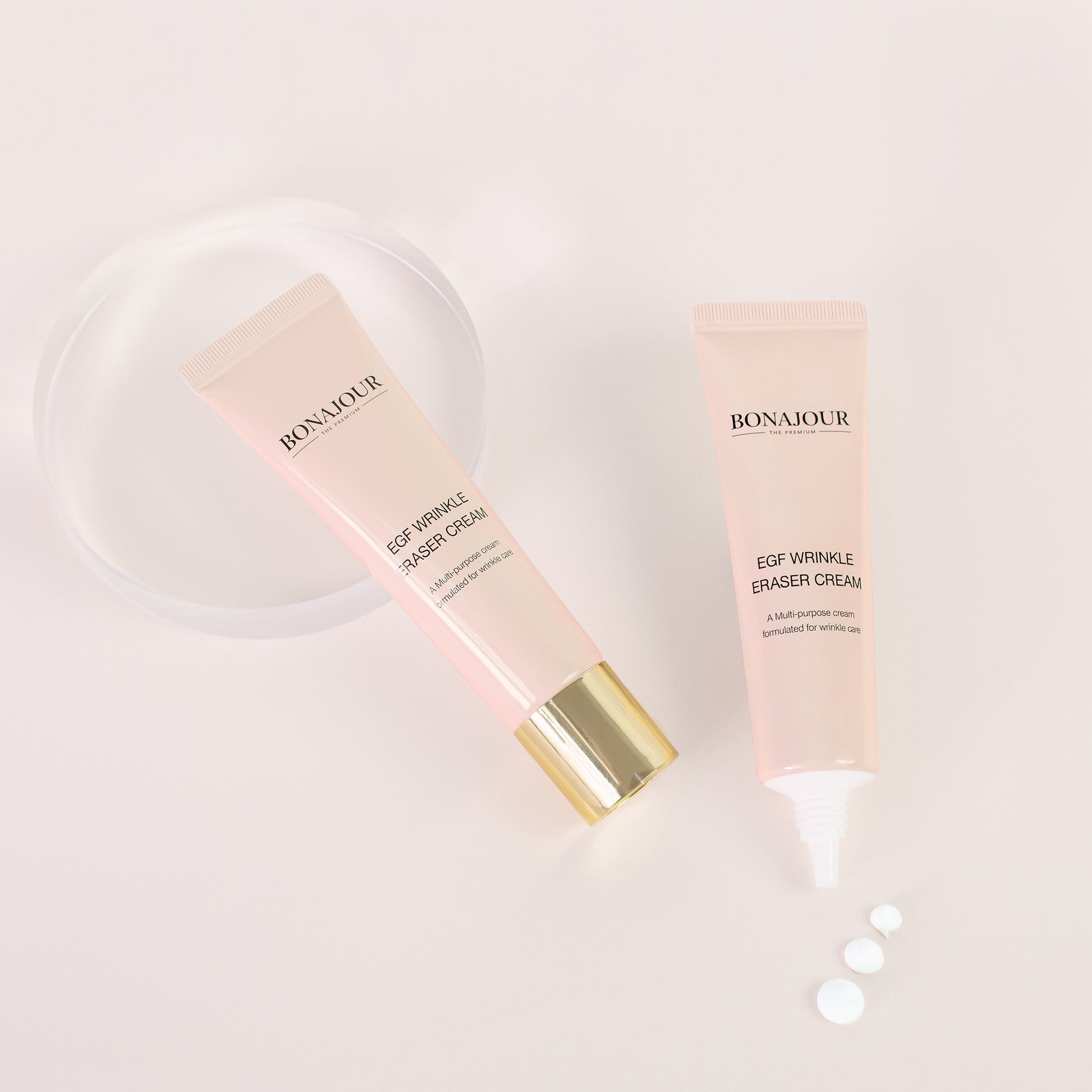Two pink tubes of Bonajour EGF Wrinkle Eraser Cream with one open and small dots of cream next to it, set on a light pink background with a circular acrylic prop.