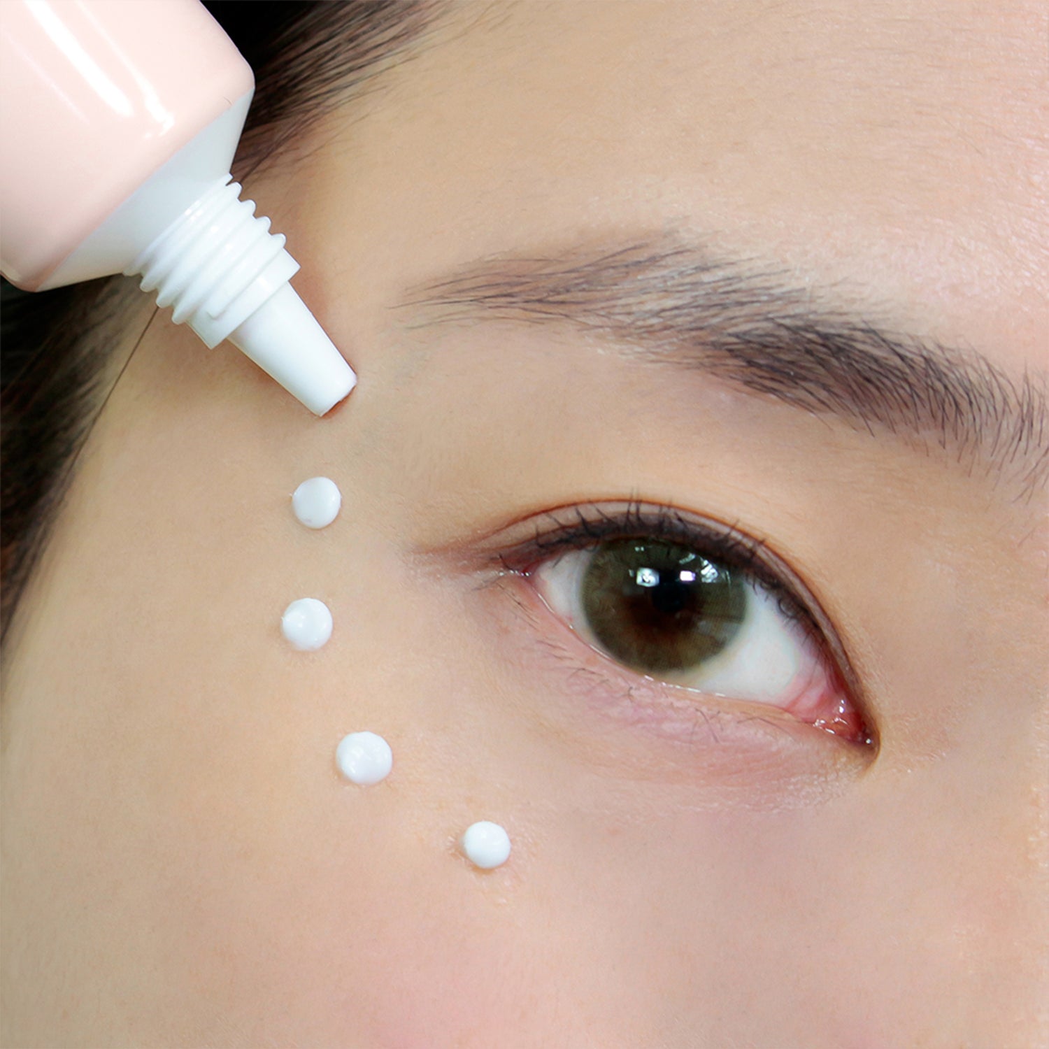 Close-up of a person's eye area with four small dots of cream being applied beneath the eye, using a tube applicator.
