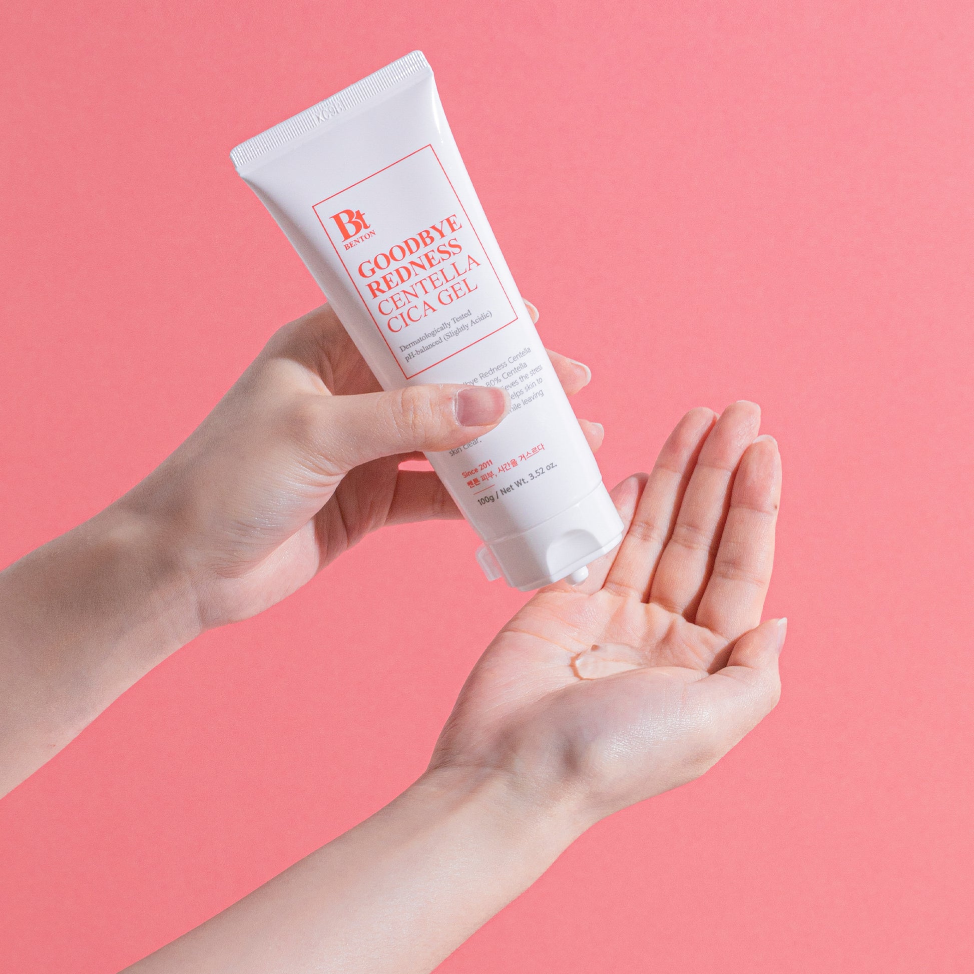 Benton Goodbye Redness Centella Cica Gel being applied from tube in hand against pink background