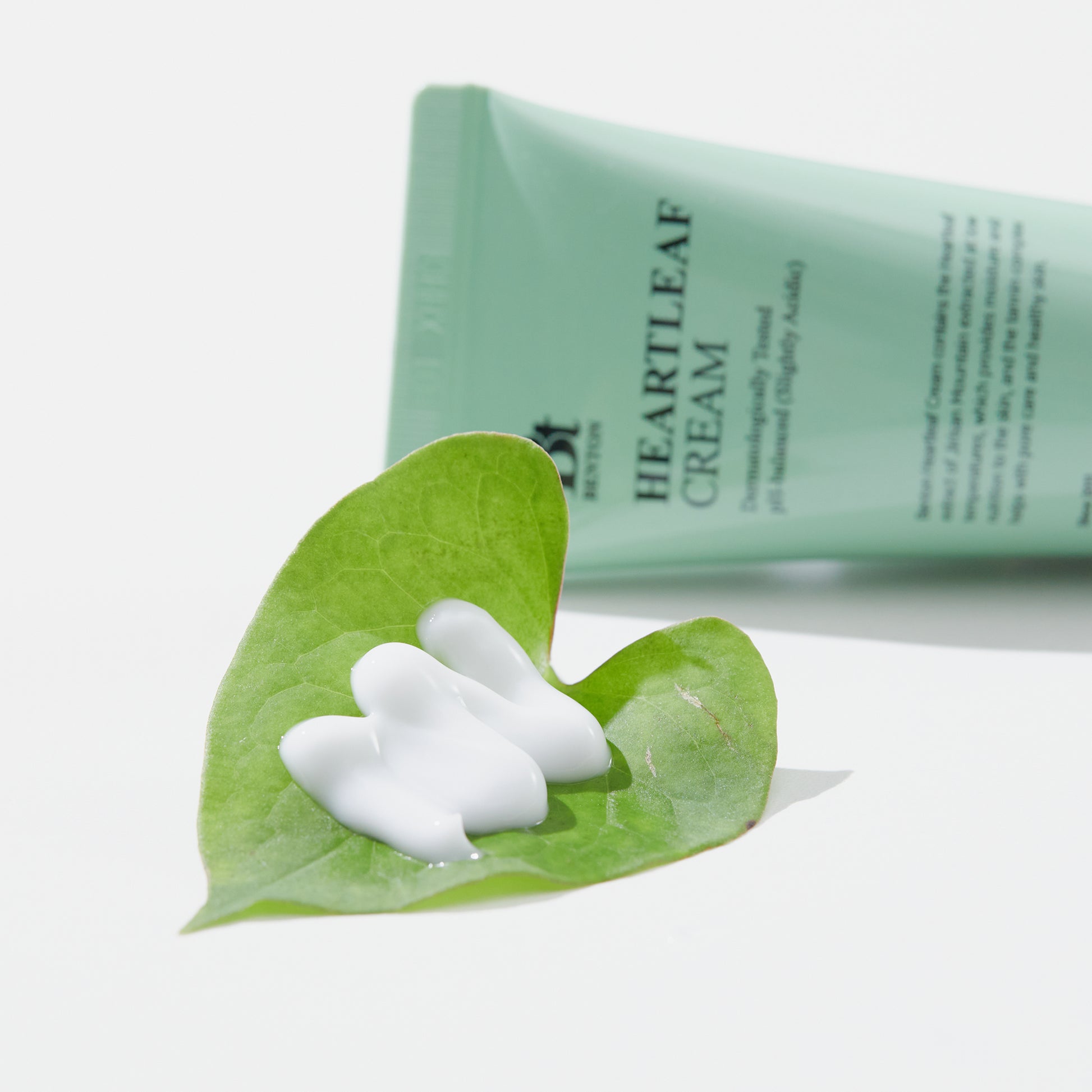 Dt Heartleaf Cream tube with product on green leaf, promoting natural skincare.