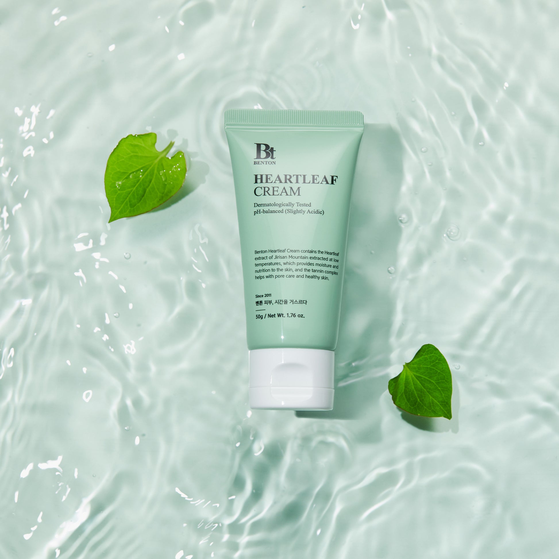 Benton Heartleaf Cream tube on watery background with green leaves, emphasizing hydration and skincare benefits.