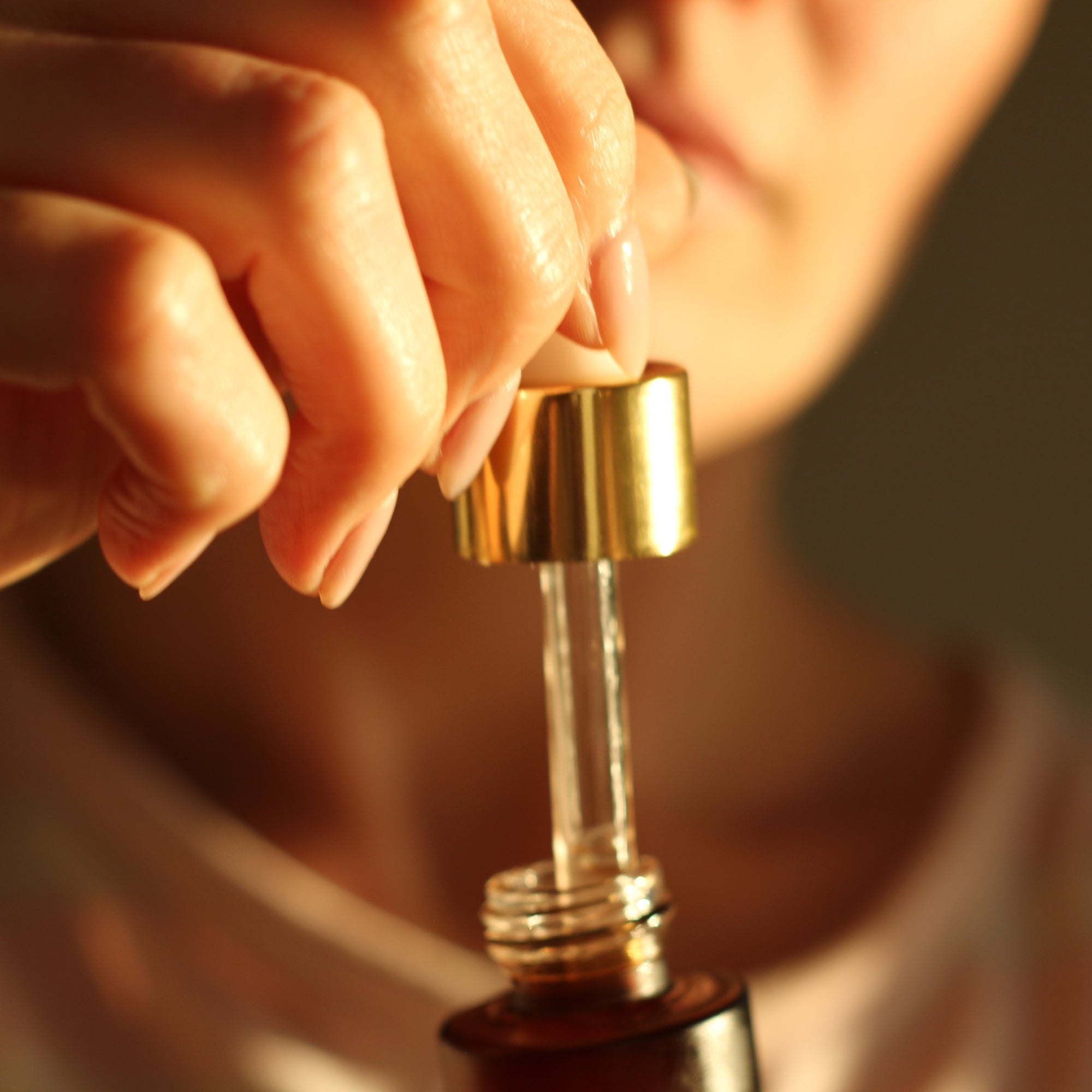 Close-up of a hand holding a gold cap on a glass bottle with a blurred background