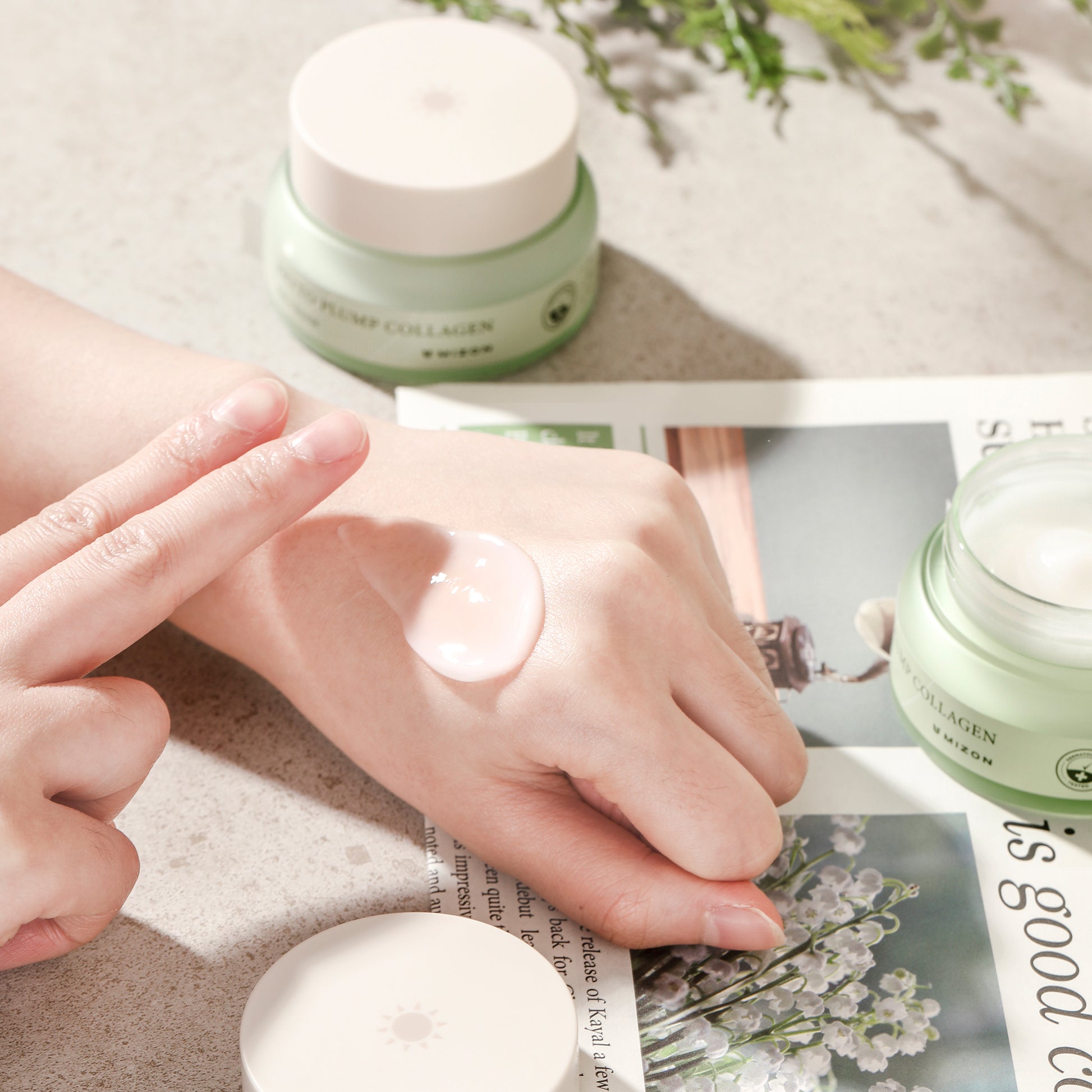 Hand applying Phyto Plump Collagen Day Cream by Mizon from an open jar on a countertop.