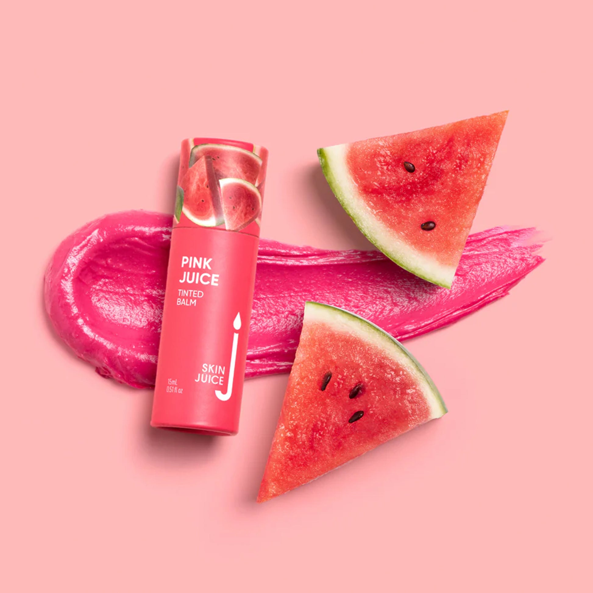 A tube of Skinjuice Pink Juice Tinted Balm displayed with watermelon slices and a smear of pink balm on a pink background.