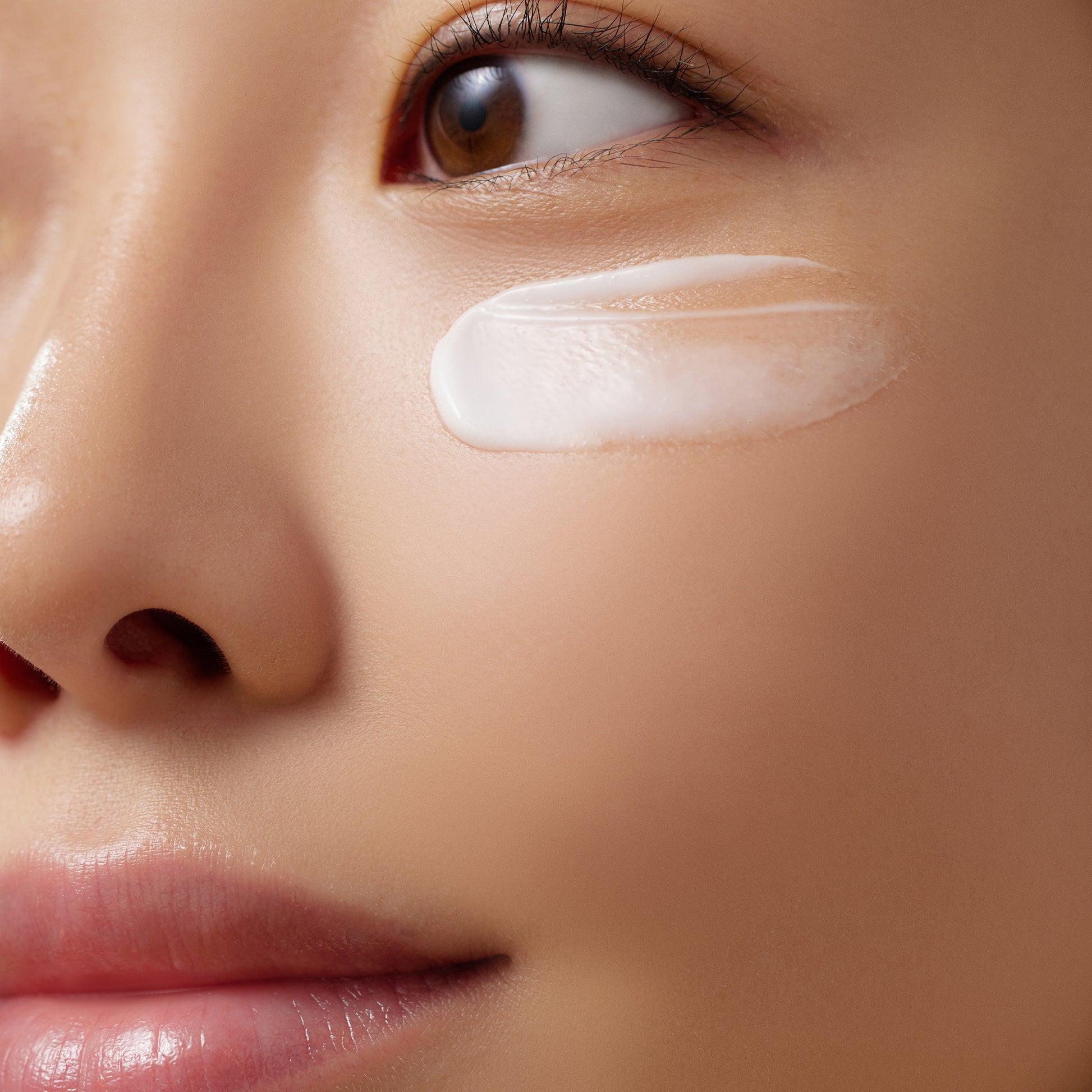Close-up of a woman's face with a swipe of cream applied under her eye, showcasing smooth skin and natural makeup.
