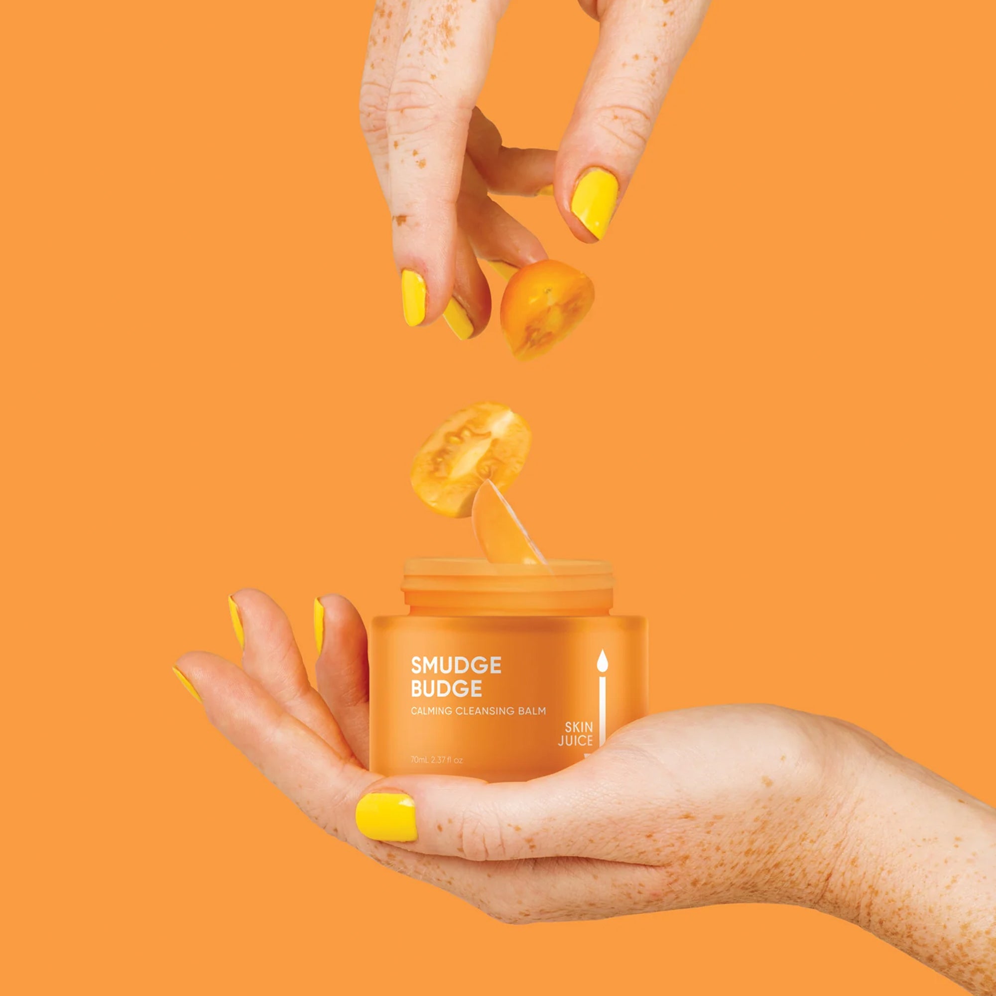 Skin Juice Smudge Budge cleansing balm with sliced tomatoes held by hands with yellow nails.