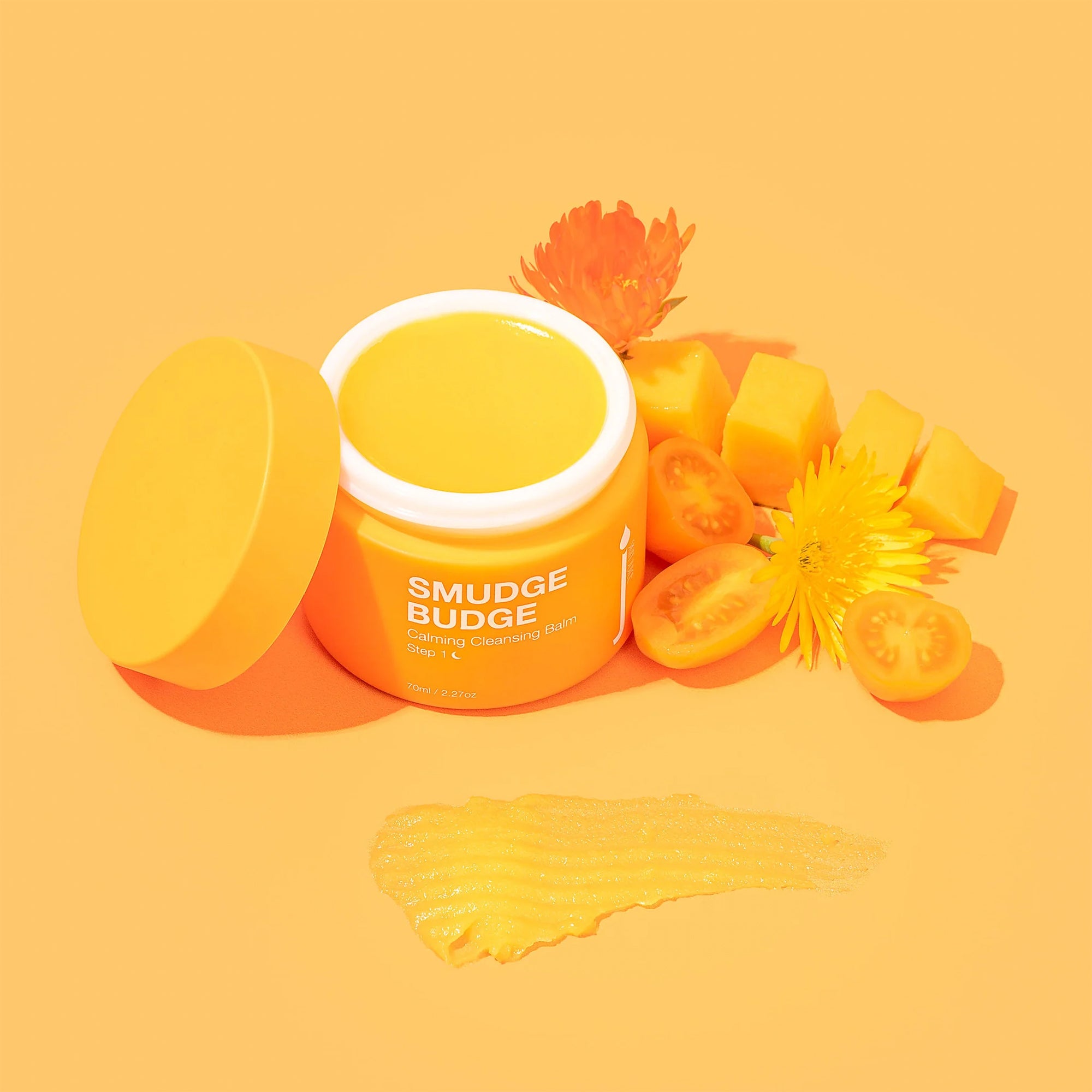 Smudge Budge Calming Cleansing Balm with florals and fruit on orange background.