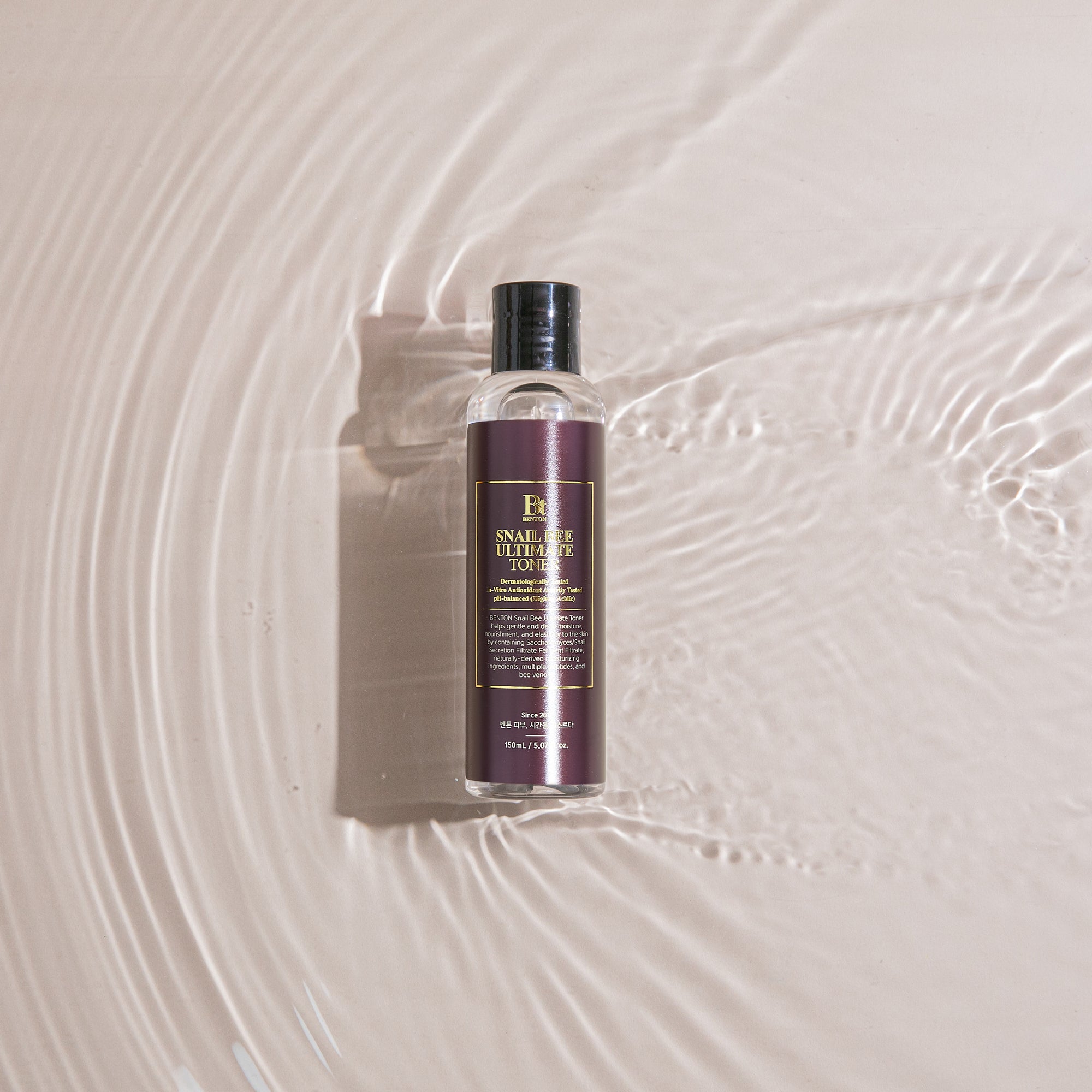 Benton Snail Bee Ultimate Toner in a clear bottle on rippling water surface.