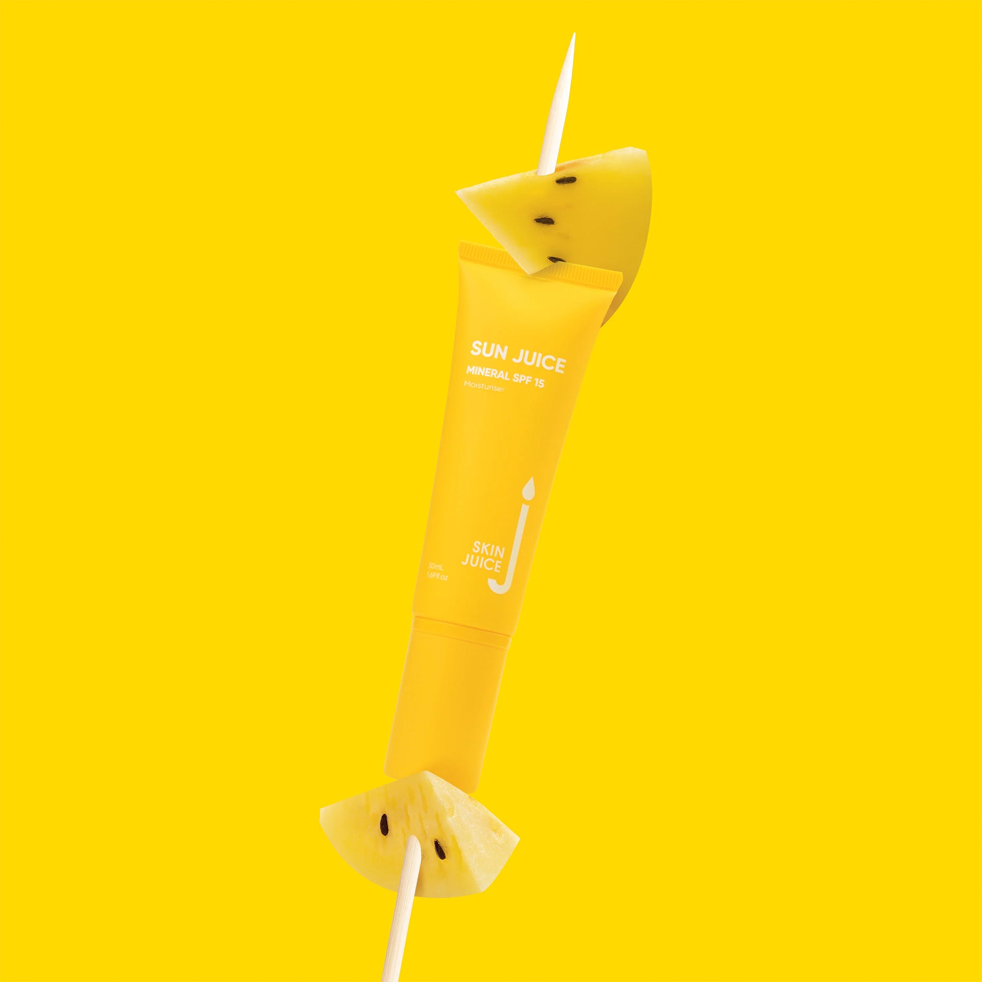 A yellow tube of Skin Juice Sun Juice Mineral SPF 15 positioned vertically, skewered with pineapple slices, against a bright yellow background.