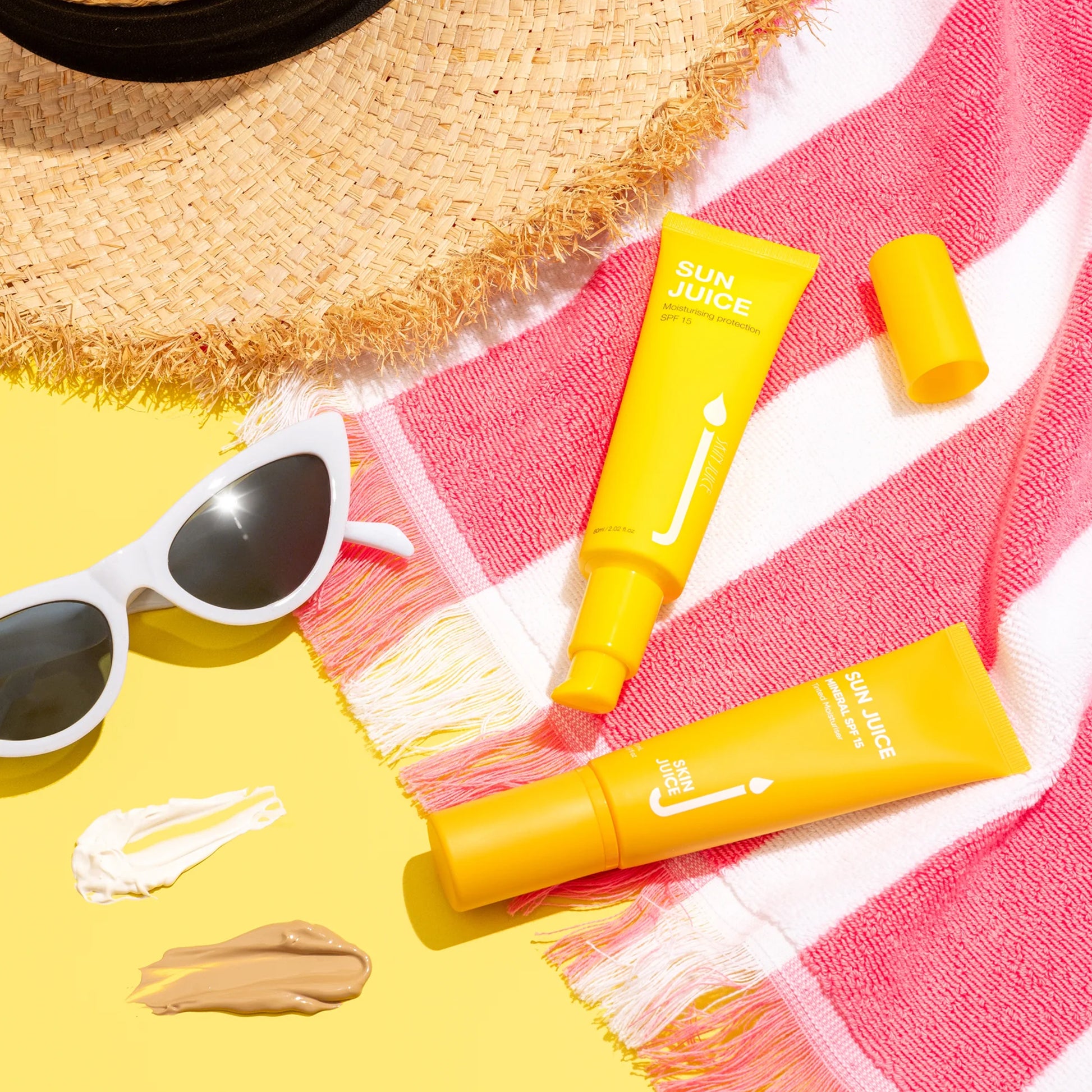 Sun Juice Untinted SPF 15 tubes on striped towel with sunglasses and straw hat.