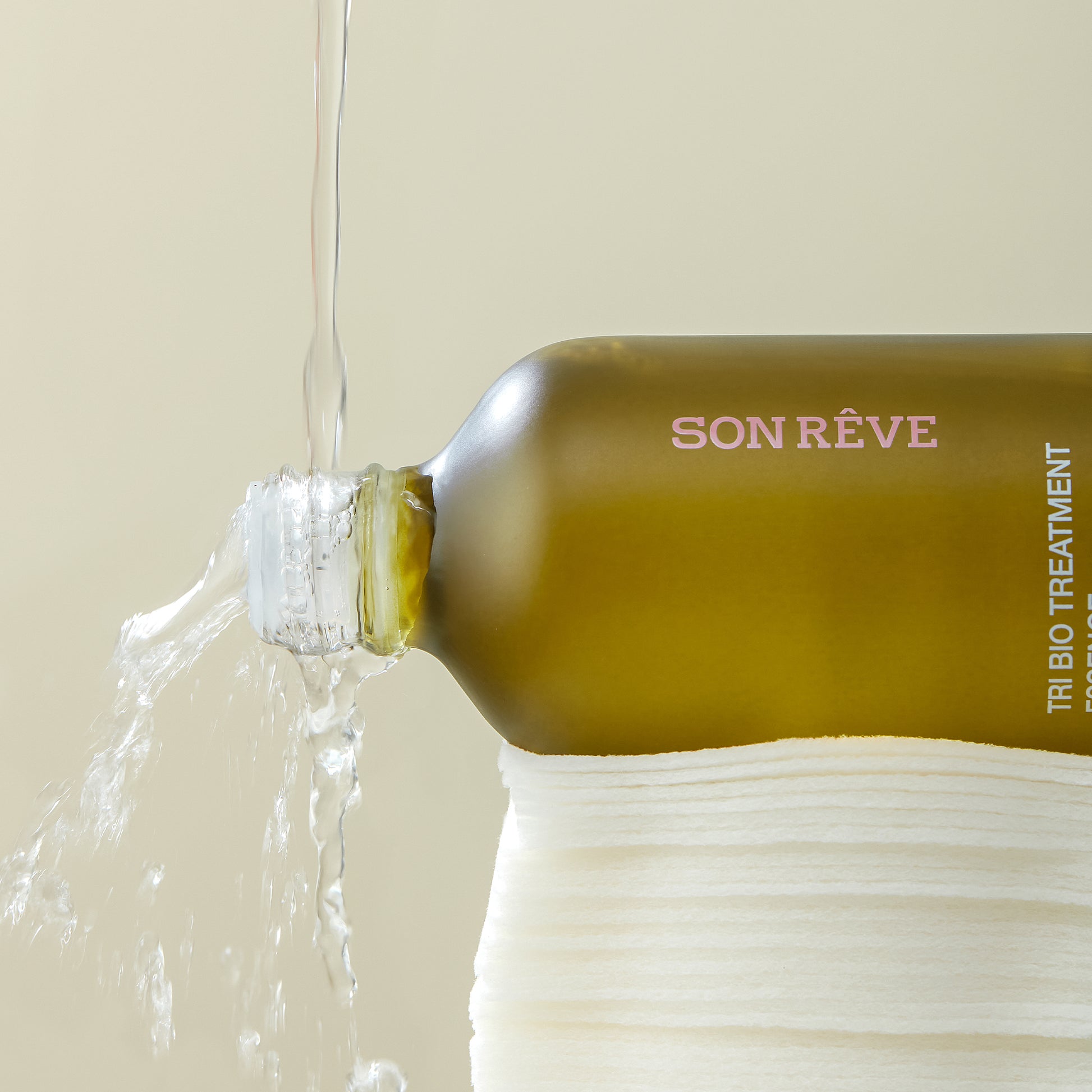 Son Rêve Tri-Bio Treatment Essence bottle with water pouring out, placed on towels.