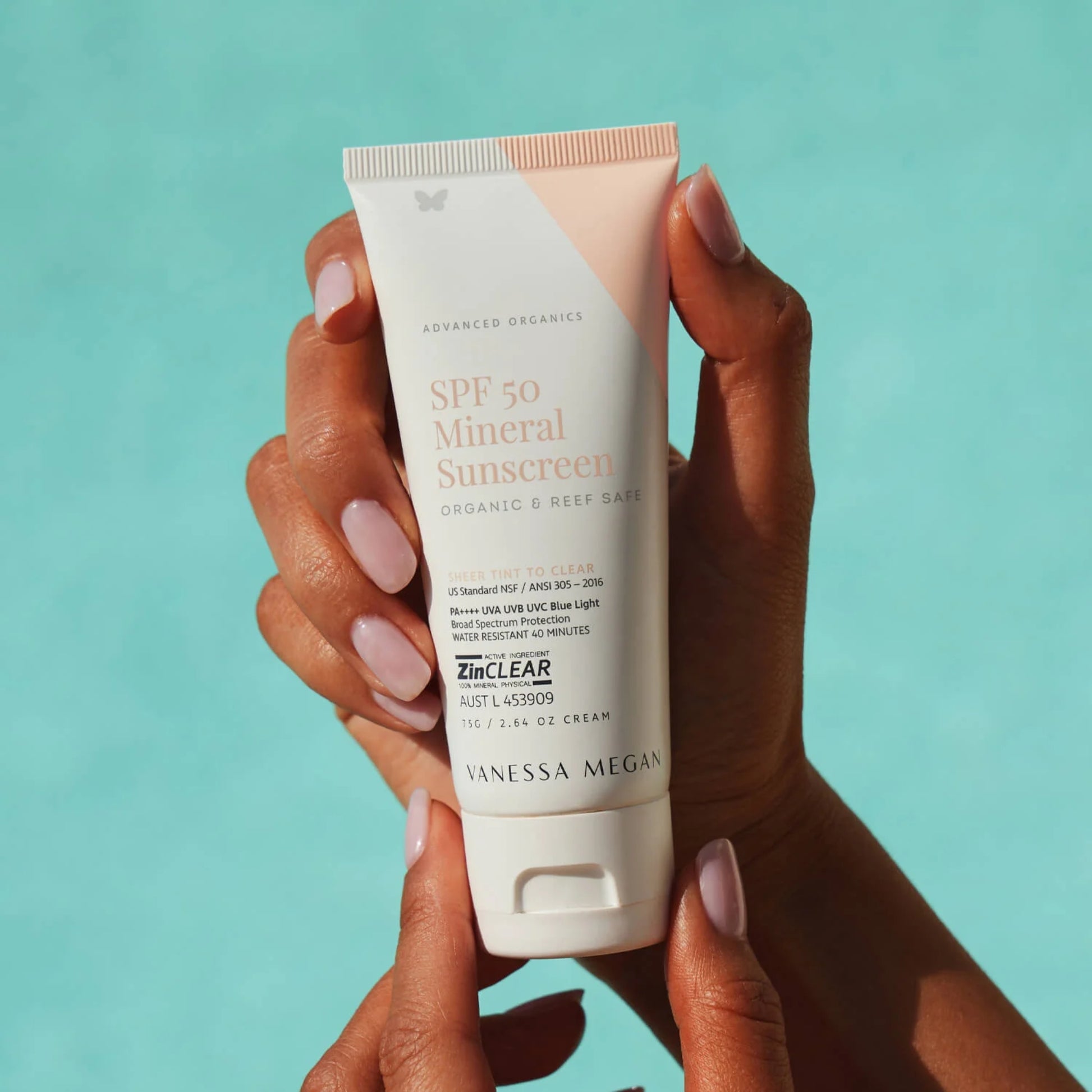 Hand holding a tube of SPF 50 mineral sunscreen against a teal background