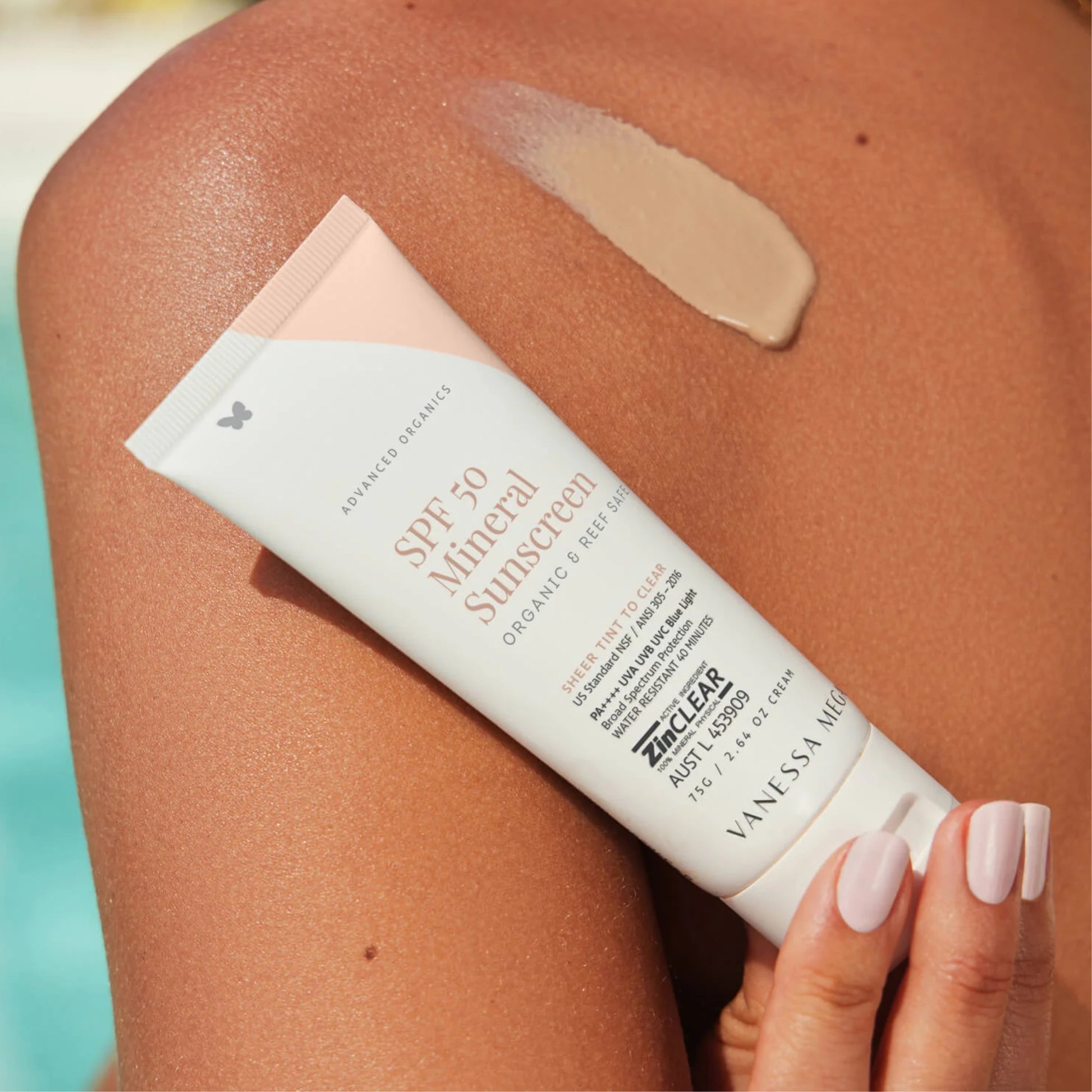 Vanessa Megan sunscreen tube being applied to a person's skin with a pool in the background