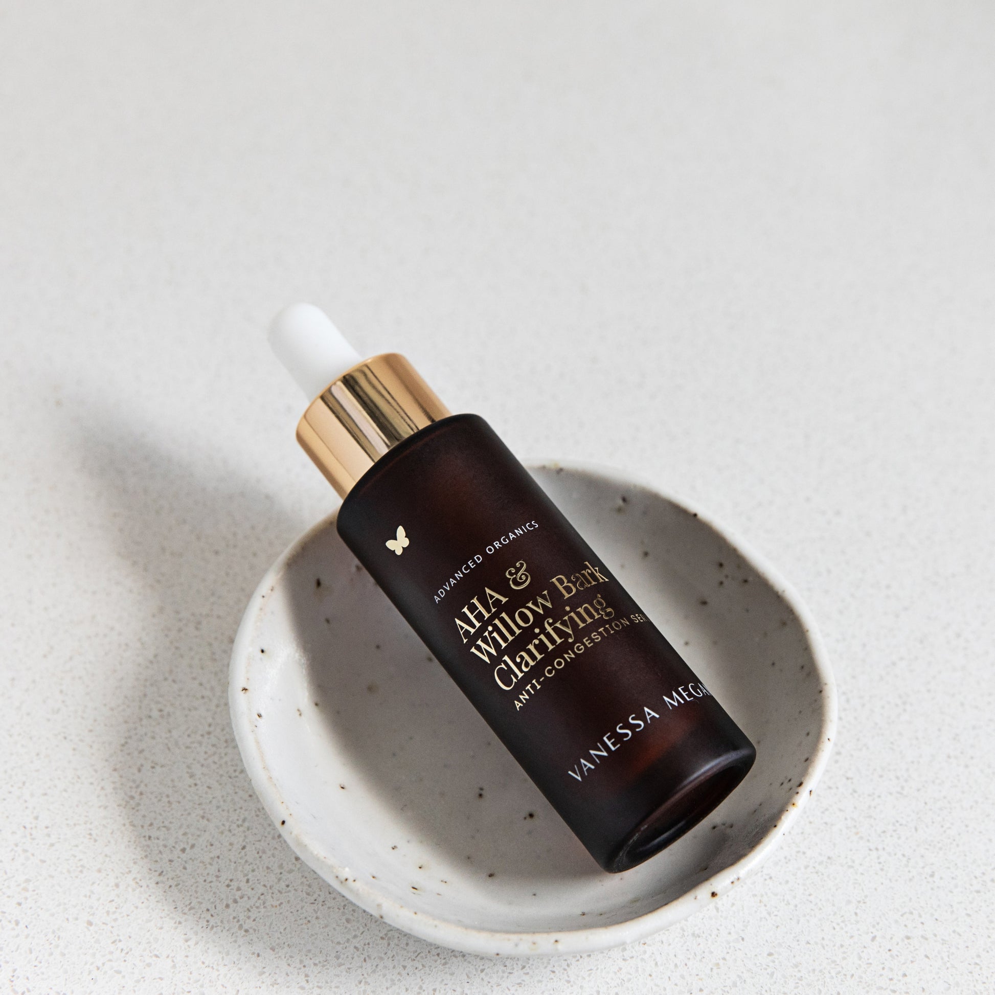 A bottle of Vanessa Megan AHA & Willow Bark Clarifying Anti-Congestion Serum on a textured white surface