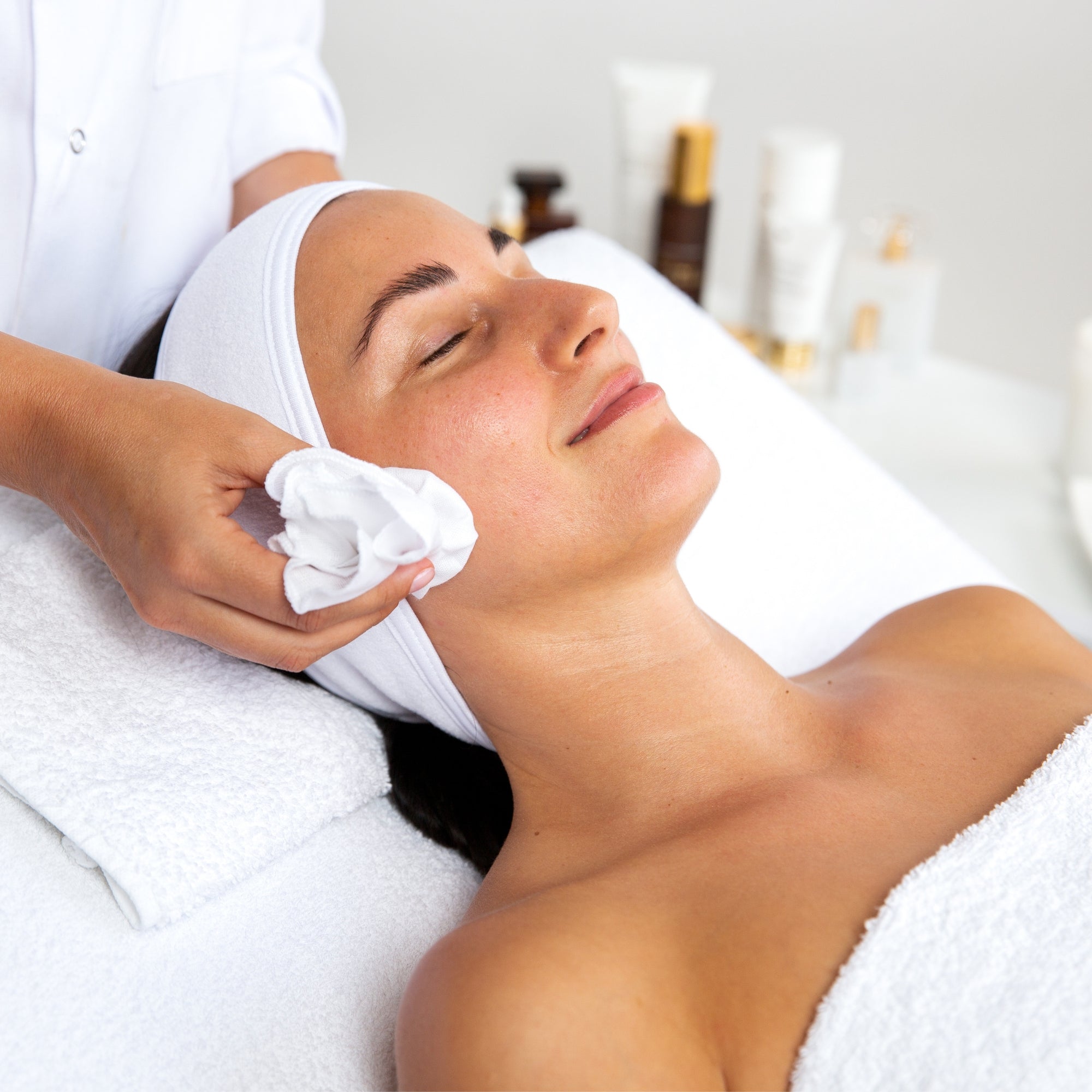 Woman receiving a facial treatment of Vanessa Megan Cryo Facelift ice cube  with a towel on her head in a spa setting
