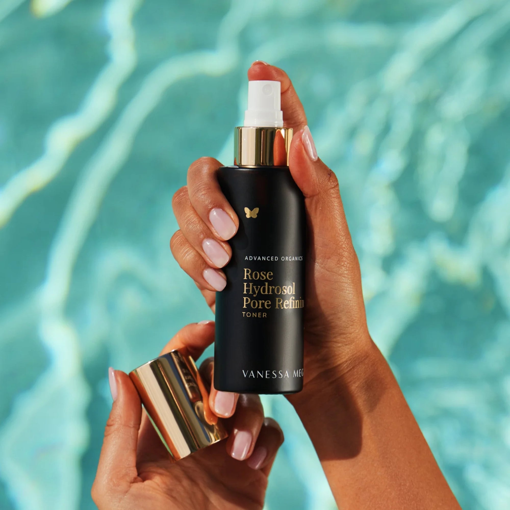 Hand holding a black bottle of Vanessa Megan Rose Hydrosol Pore Refining Toner with a blurred pool background