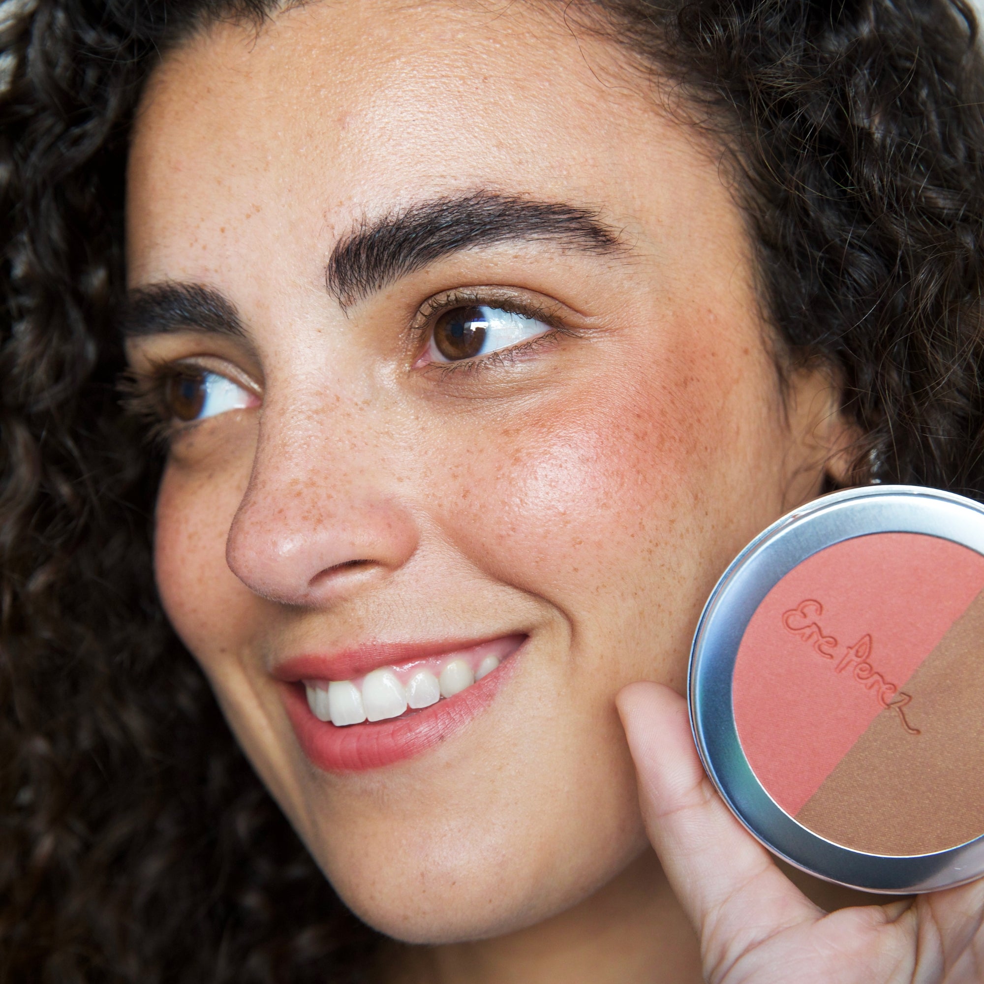 A smiling lady with a palate of Ere Perez blush in Brooklyn colour