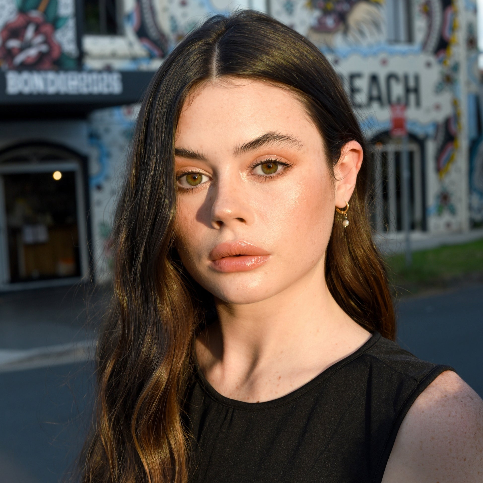 Woman with long brown hair and wearing a black top, looking into the camera. She has subtle makeup with emphasis on the cheeks, possibly using the Rice Powder Blush.