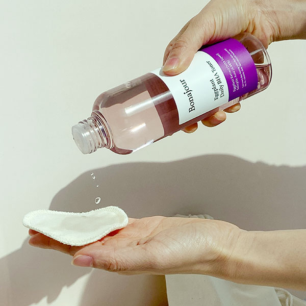 Person pouring the Eggplant Daily BHA Toner from a bottle onto a cotton pad.