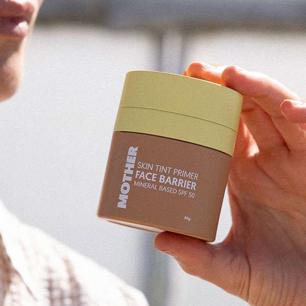 Close-up of a person holding a jar of Face Barrier SPF50 with the label visible, showcasing its high sun protection factor.