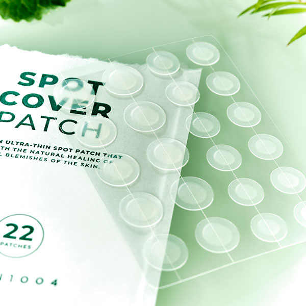 A pack of Tea-Trica Spot Cover Patch, featuring 22 circular pieces to treat skin blemishes, shown with green leaves in the background.